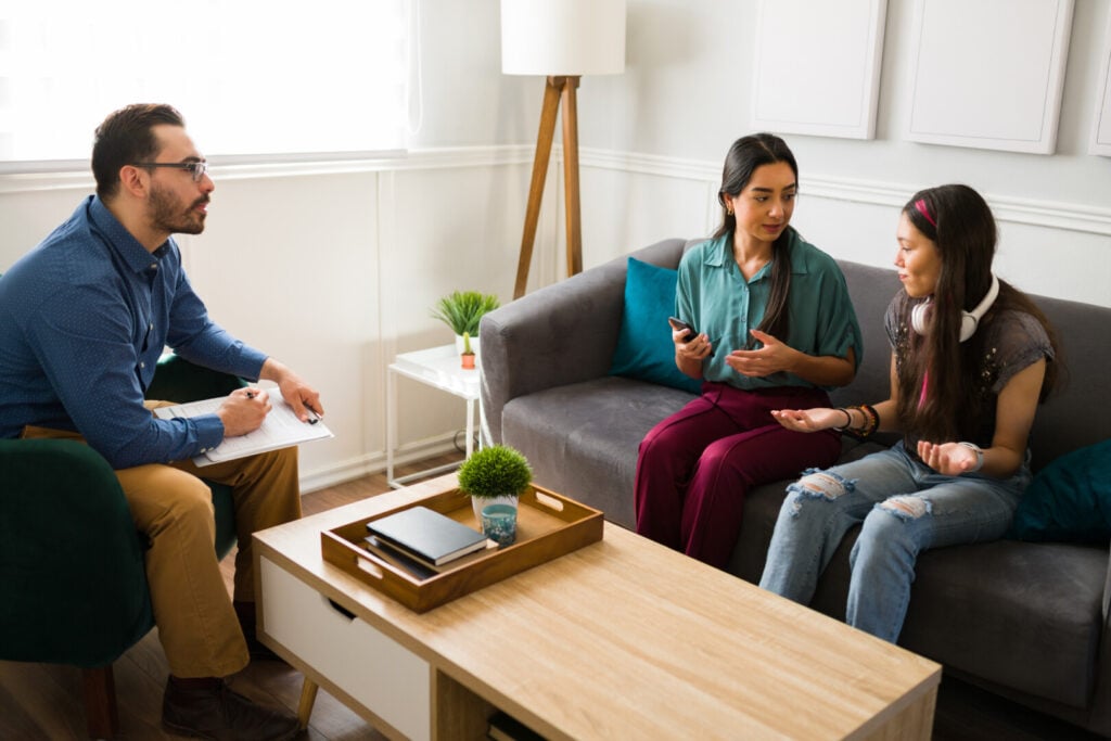 A male therapist facilitates a family counseling session with a mother and her teenage daughter