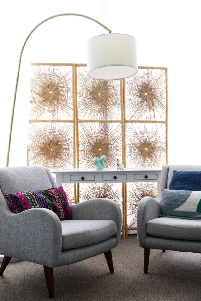 A modern therapy office with two grey armchairs, a decorative screen, and an arc floor lamp.