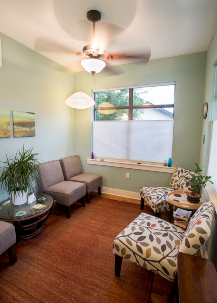 A calm therapy office waiting room with light green walls, comfortable chairs, and house plants.