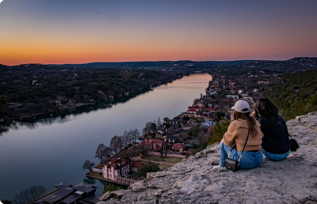 Two people watch the sunset from an overlook above the Colorado River in Austin.