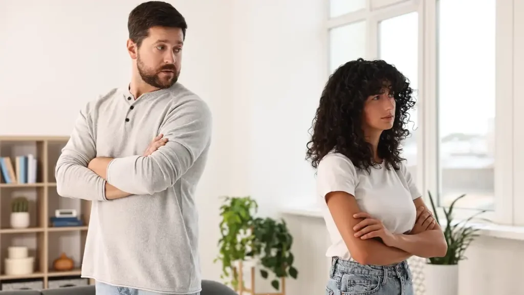 A couple standing apart with their arms crossed, looking away from each other during a disagreement.